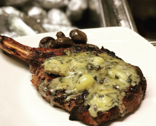 A grilled steak topped with melted cheese, served with sautéed mushrooms on a white plate.