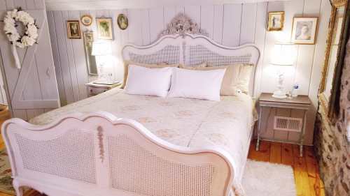 Cozy bedroom featuring a vintage white bed, soft bedding, and framed artwork on the walls. Warm lighting from lamps.