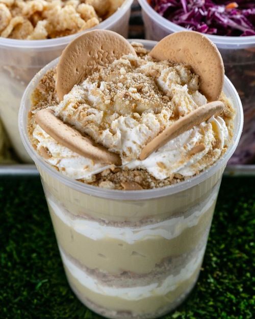 A layered dessert in a clear cup, featuring cream, crumbled cookies, and topped with whipped cream and cookie halves.