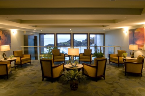 Cozy lounge area with armchairs, lamps, and large windows overlooking a scenic view of the ocean.