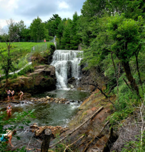 A scenic waterfall surrounded by lush greenery, with people enjoying the water at the base.