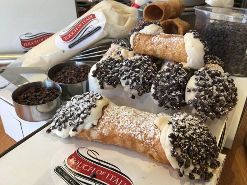 A display of cannoli filled with cream and topped with chocolate chips, alongside bags of ingredients and chocolate sprinkles.