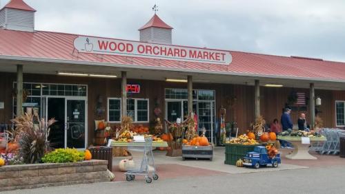 Exterior of Wood Orchard Market with pumpkins and fall decorations, shoppers at the entrance, and a red roof.