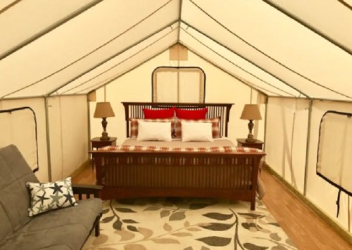 Cozy glamping tent interior featuring a bed, two lamps, and a seating area with a patterned rug.
