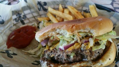 A close-up of a burger with lettuce, cheese, and onions, served with fries and a side of ketchup.
