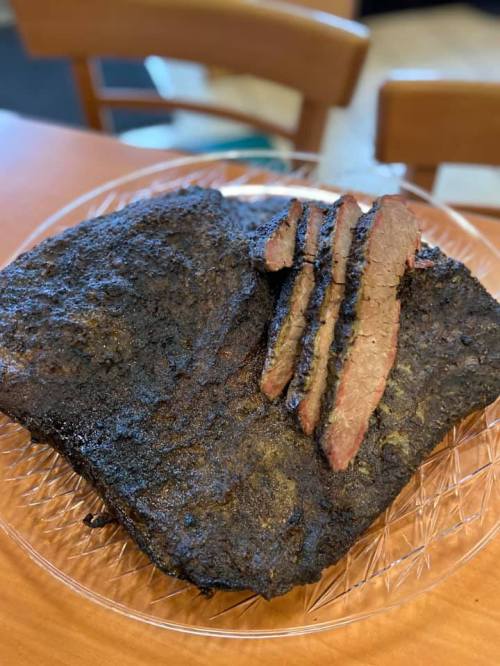A plate of smoked brisket, featuring a thick, charred exterior and several slices cut from the top.