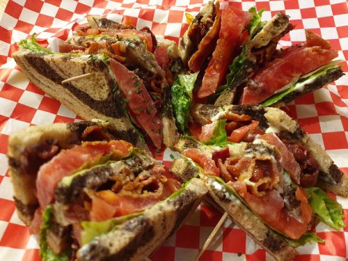 A close-up of a sliced sandwich with layers of bacon, lettuce, and tomato on toasted brown bread, served on a checkered plate.