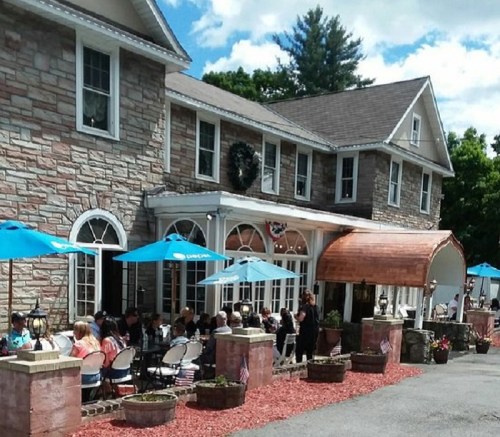 A stone building with outdoor seating under blue umbrellas, filled with diners enjoying a sunny day.