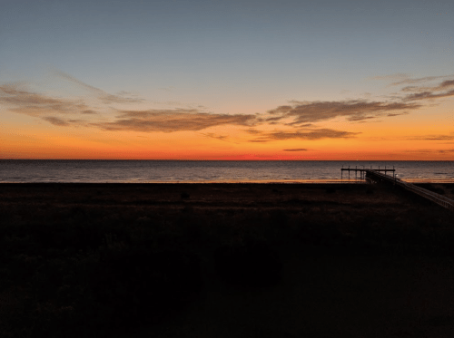 A serene sunset over the ocean, with vibrant orange and blue hues and a pier extending into the water.