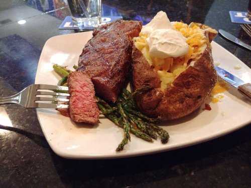 A plate with a medium-rare steak, baked potato topped with cheese and sour cream, and asparagus on the side.