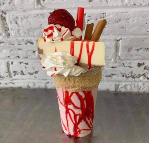 A tall milkshake topped with whipped cream, a strawberry, chocolate sticks, and drizzled with red syrup.