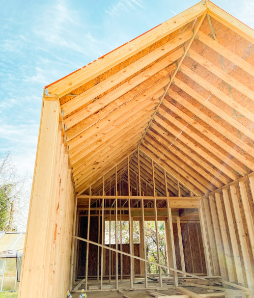 Interior view of a wooden structure under construction, showcasing exposed beams and framing against a blue sky.