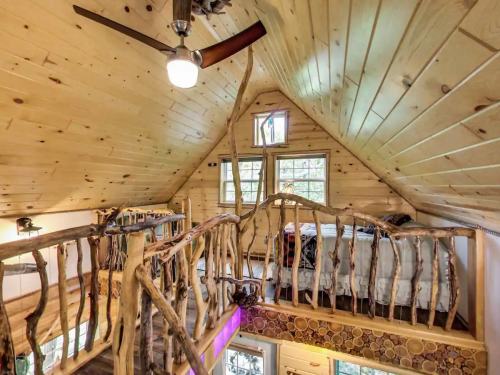 Cozy wooden interior of a cabin with a loft, featuring natural wood beams and a unique railing design.