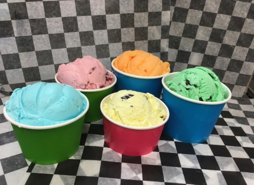 Five colorful ice cream scoops in cups: blue, pink, orange, yellow, and green, set against a checkered background.