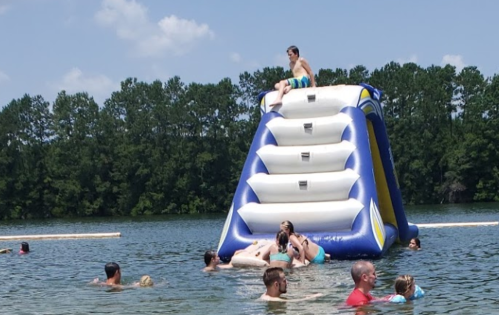 A group of people enjoying a sunny day at a lake, with an inflatable water slide and swimmers around it.