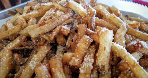 A close-up of a pile of golden-brown French fries sprinkled with seasoning.