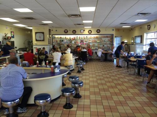 A busy diner interior with patrons seated at tables and a counter, featuring colorful decor and a display of collectibles.