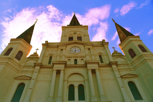 A tall church with three spires against a vibrant sky, featuring a clock and intricate architectural details.