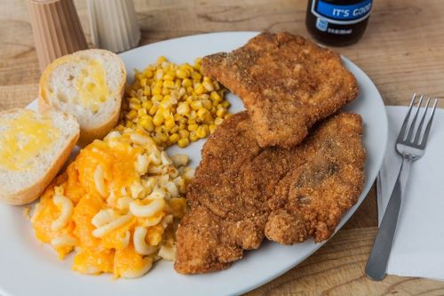 A plate of fried chicken, macaroni and cheese, corn, and two slices of buttered bread.