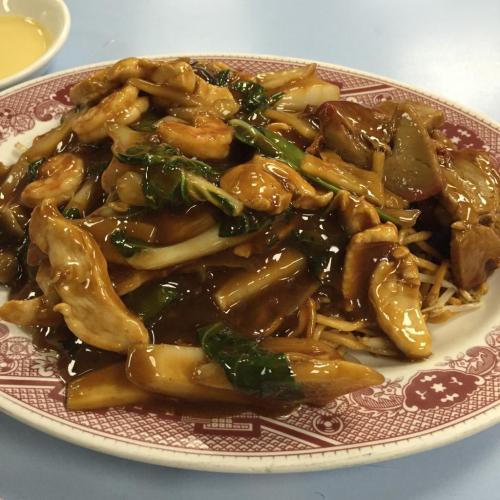A plate of stir-fried noodles with chicken, shrimp, and vegetables in a savory brown sauce.