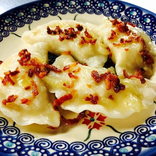 A plate of dumplings topped with crispy bits of bacon, served on a decorative blue and white patterned dish.