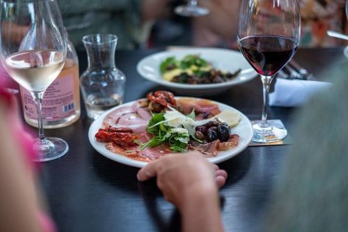 A plate of assorted cured meats, olives, and greens, with glasses of red and white wine in the background.