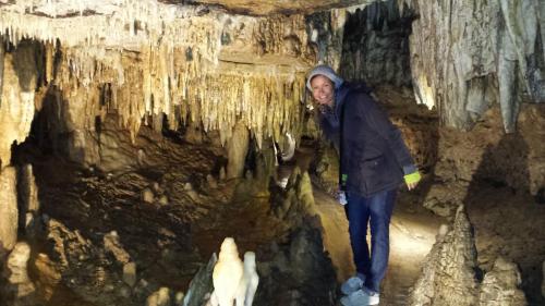 A person stands in a cave surrounded by stalactites and stalagmites, with dim lighting illuminating the rocky formations.