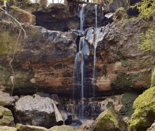 A serene waterfall cascading over rocky cliffs, surrounded by lush greenery and moss-covered stones.