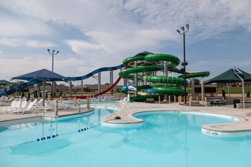 A water park featuring a large pool, water slides, and lounge chairs under shaded areas.