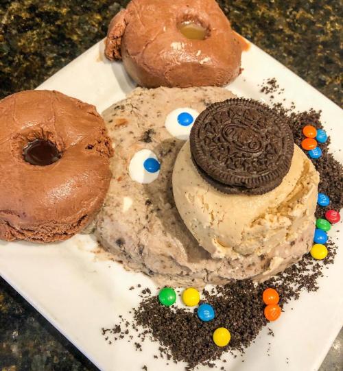 A plate with two chocolate donuts, a scoop of cookies and cream ice cream, an Oreo, and colorful candy pieces.