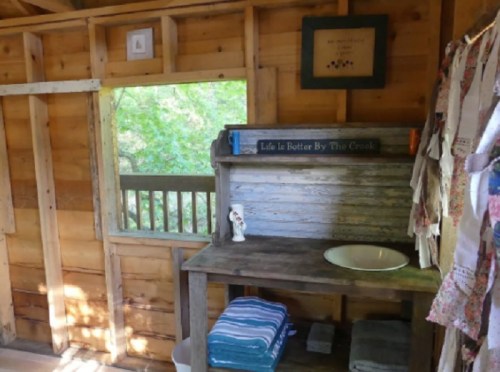 Cozy wooden interior with a sink, shelves, and a window overlooking greenery. Decorated with towels and a framed quote.