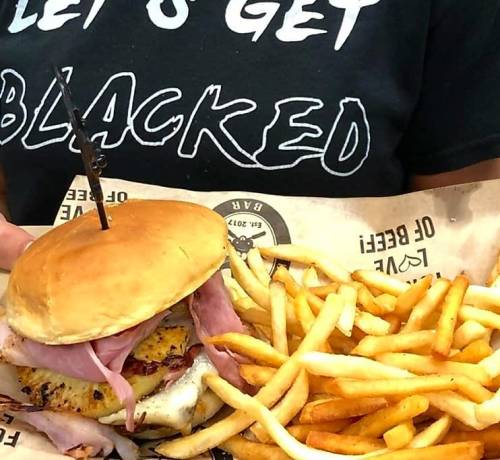 A person holds a sandwich with ham and cheese, accompanied by a side of golden French fries.