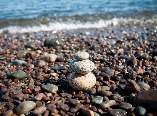 A stack of smooth stones on a pebbly beach, with gentle waves lapping at the shore in the background.