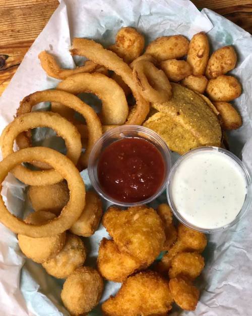 A platter of fried snacks including onion rings, hushpuppies, and dipping sauces.