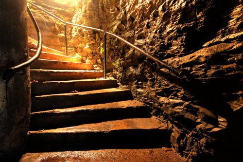 A dimly lit stone staircase leads upward, illuminated by warm light filtering from above.