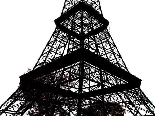Silhouette of a tower with intricate metal framework against a white background, featuring some foliage at the base.