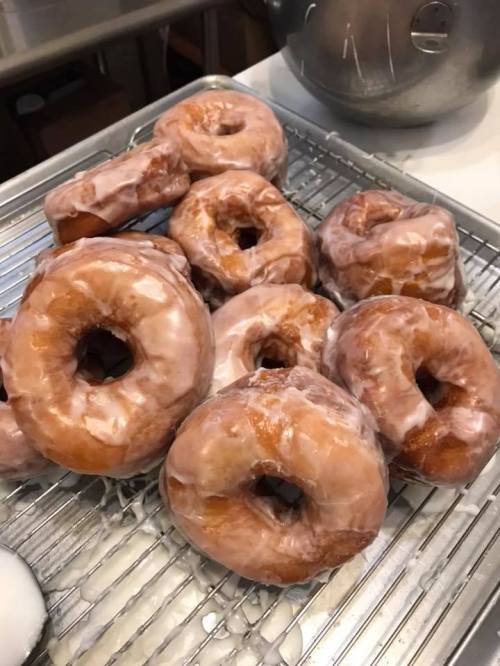 A tray of freshly glazed donuts, some stacked and others laid out, glistening with a sugary coating.