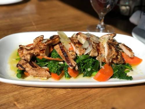 Grilled chicken strips on a bed of sautéed vegetables, including carrots and broccolini, drizzled with sauce.
