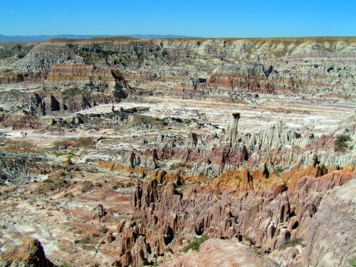 A vast, colorful landscape of eroded rock formations and mesas under a clear blue sky.