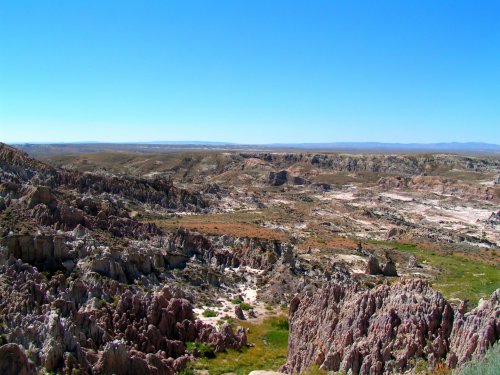 A vast, arid landscape with colorful rock formations and sparse vegetation under a clear blue sky.