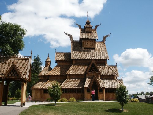 A wooden, intricately designed building with a steep roof and decorative spires, set against a blue sky with clouds.