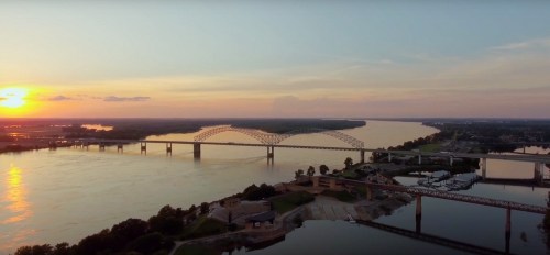 Aerial view of a river at sunset, featuring a bridge and waterfront with boats along the shore.