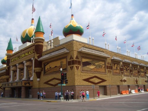 The Mitchell Corn Palace features colorful, ornate architecture with corn murals and flags, set against a cloudy sky.