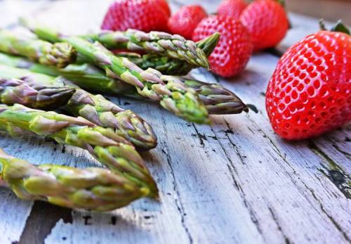 Fresh asparagus spears and ripe strawberries arranged on a rustic wooden surface.
