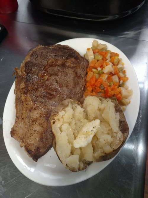 A plate with a large grilled steak, a baked potato, and a side of mixed vegetables.