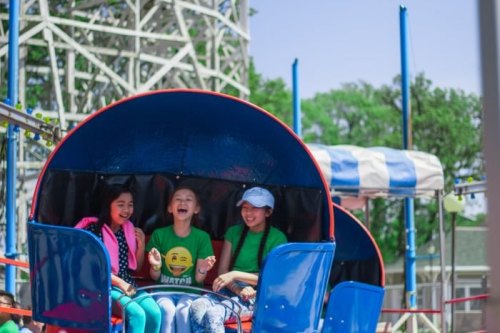 Three girls laughing together on a colorful amusement park ride, enjoying a sunny day.