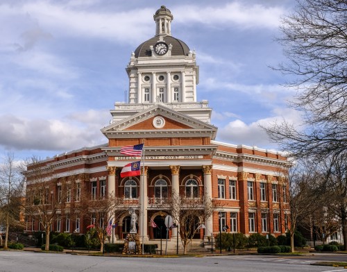 Historic building with a clock tower, featuring American flags and a grand entrance, set against a cloudy sky.