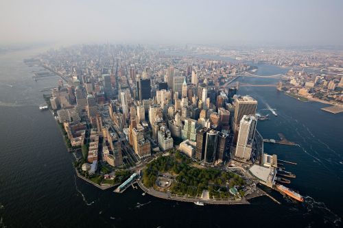 Aerial view of Manhattan, showcasing skyscrapers, waterways, and green spaces along the coastline.
