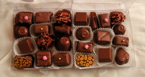 A box of assorted chocolates, featuring various shapes and toppings, arranged in paper liners.