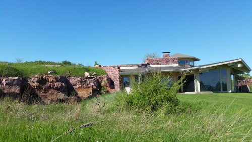 A modern house built into a rocky hillside, surrounded by green grass and clear blue skies.